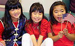 Three smiling young girls, one holding the USA flag.